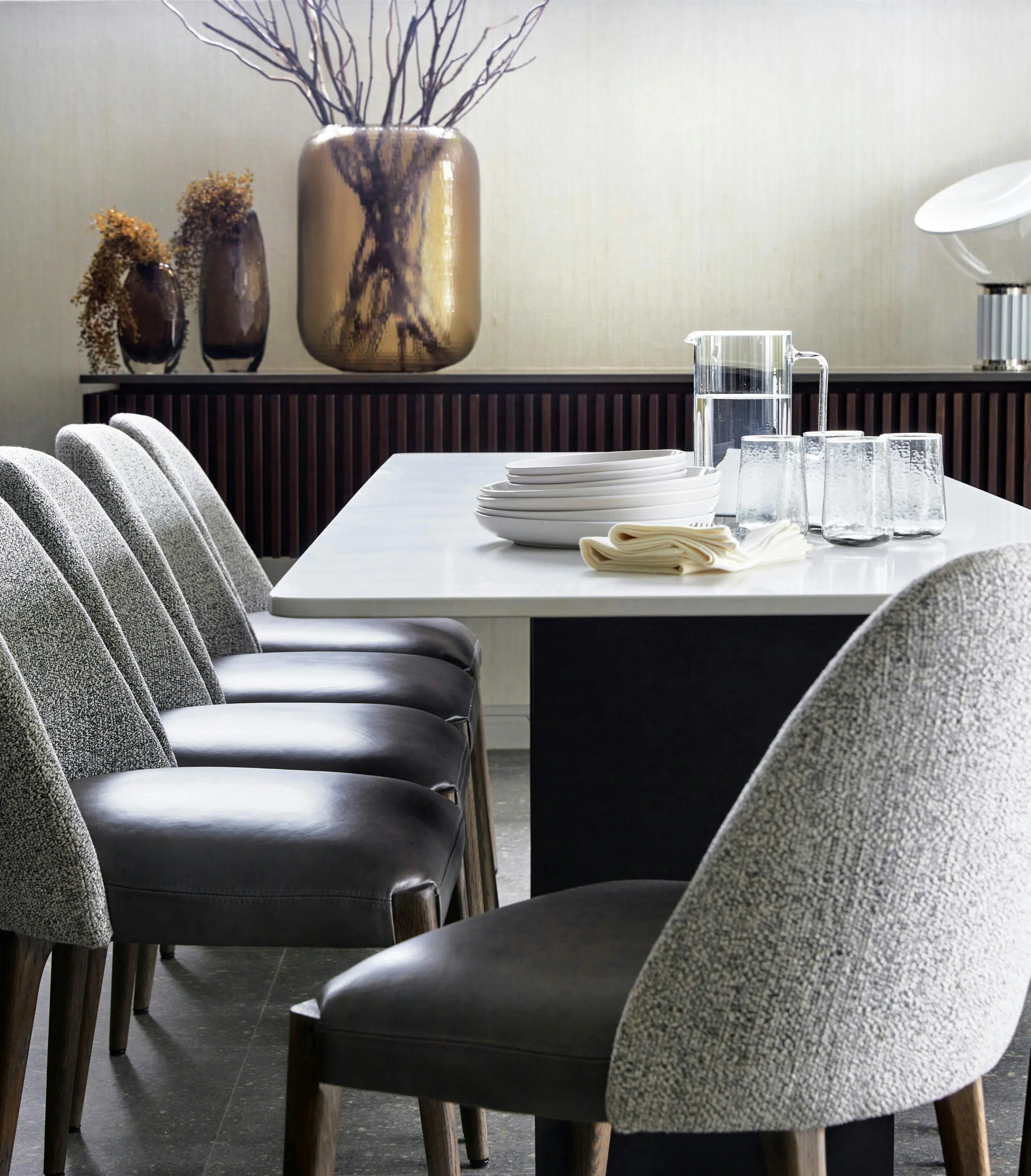 Close-up of modern, grey dining chairs, a dining table and a wooden console table with decorative accents in the background.