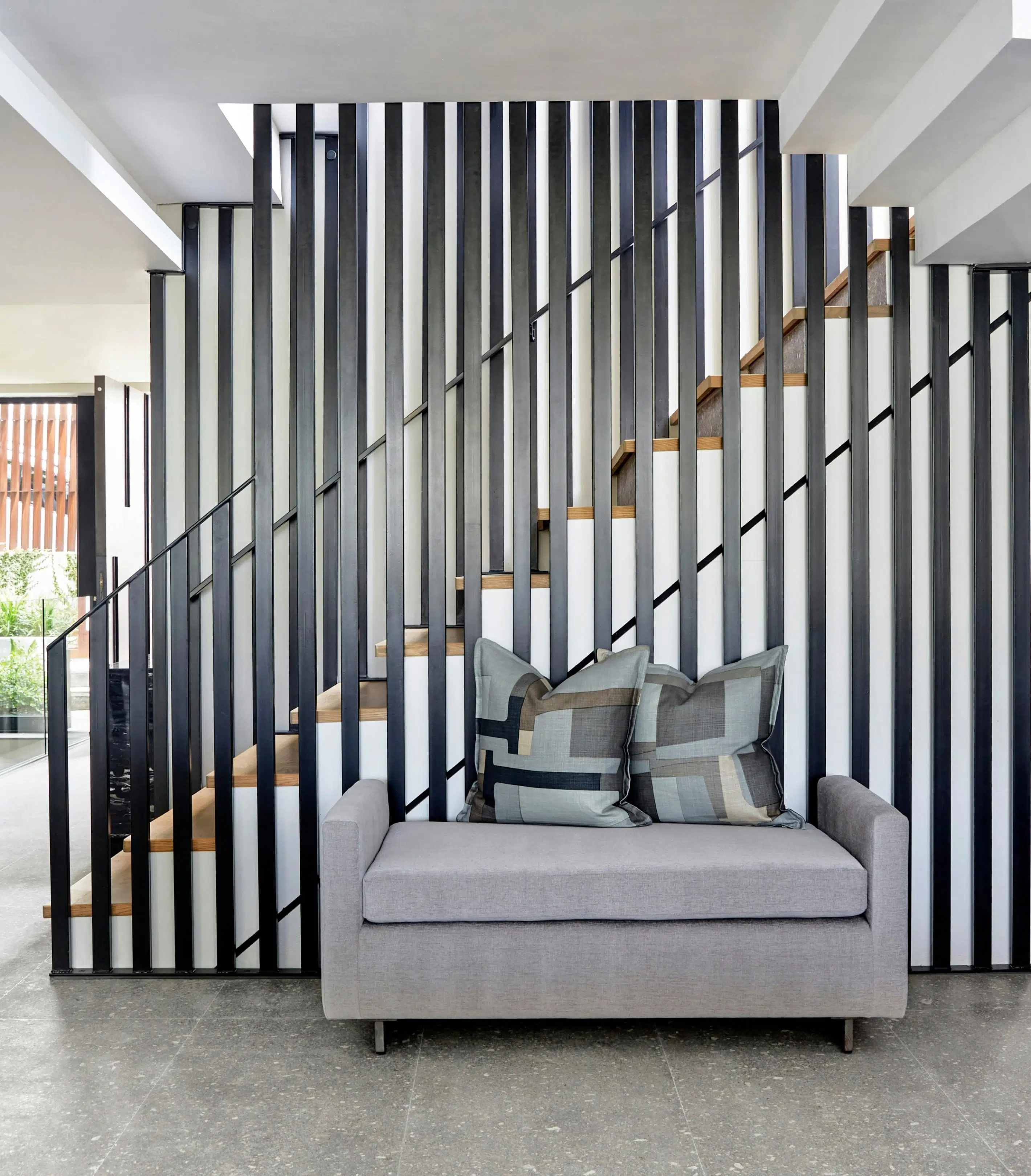 A small grey sofa sits in front of a staircase with vertical panelling in a black tone.